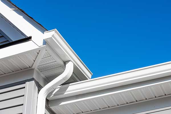 White, k-style gutter system with a downspout attached to the fascia of a residential home